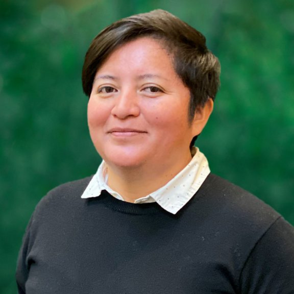 Doris Garrido wearing a dark sweater over a white shirt with a green background