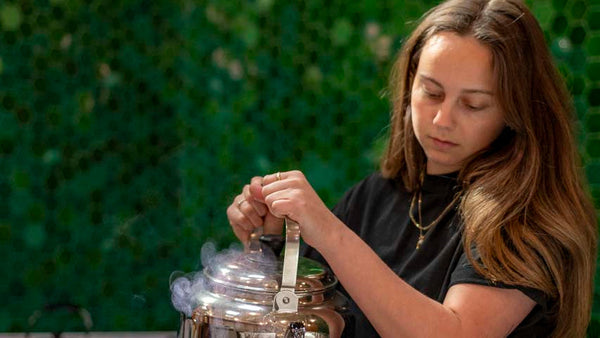 Isabella preparing to cup coffee, a green tiled wall in the background